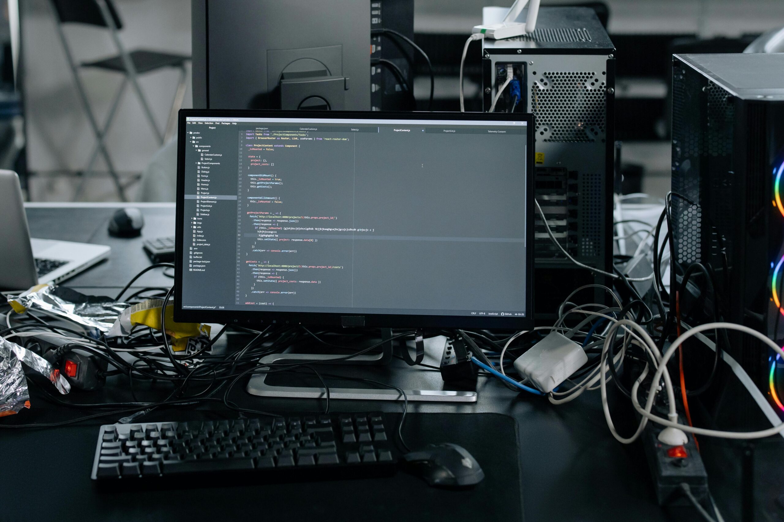 Home A cluttered workstation in an office featuring a monitor displaying code, surrounded by a keyboard, mouse, and wiring.